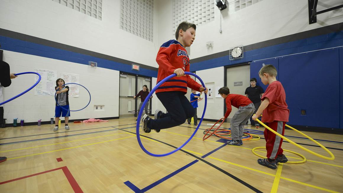 Boy jumping with hula hoop in gymnasium