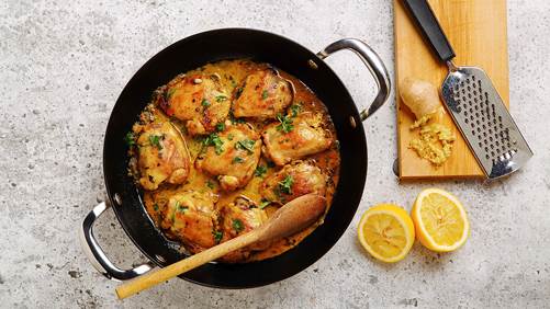 Curried lemon ginger chicken in a large skillet with grated ginger and cut lemon on the side. 