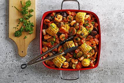 Grilled shrimp and corn casserole in a square red serving dish with tongs