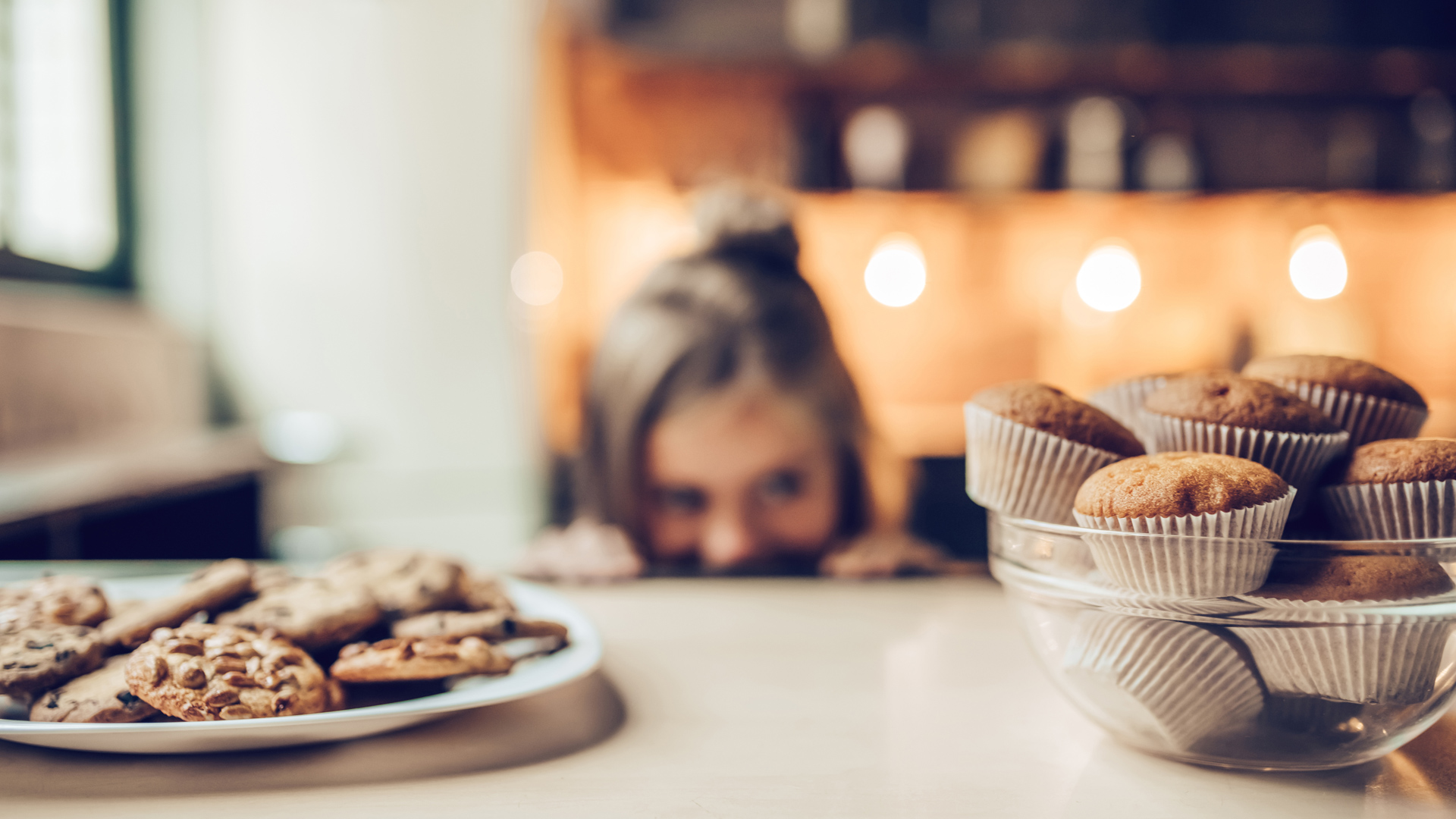 Little girl on the edge of the counter eyeing plates of cookies and muffins
