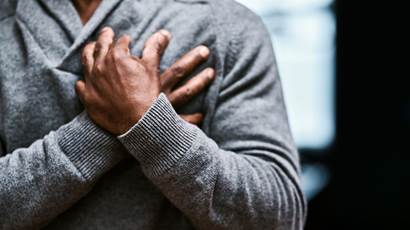 A man in a grey sweater crossing his hands over his heart.