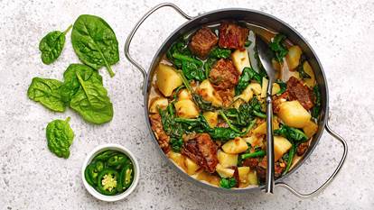 Spiced beef with spinach and potatoes in a skillet with sliced jalapenos and spinach leaves displayed on the counter beside it. 