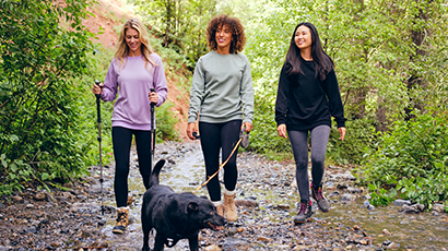 Three women walking a dog along a wooded path